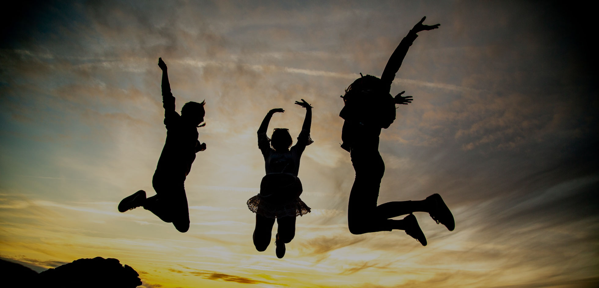 Three people jumping in the air against a sunset sky.