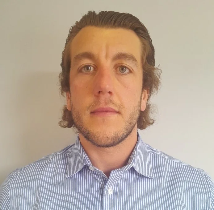 A man with light brown hair and beard wearing a blue and white striped shirt.