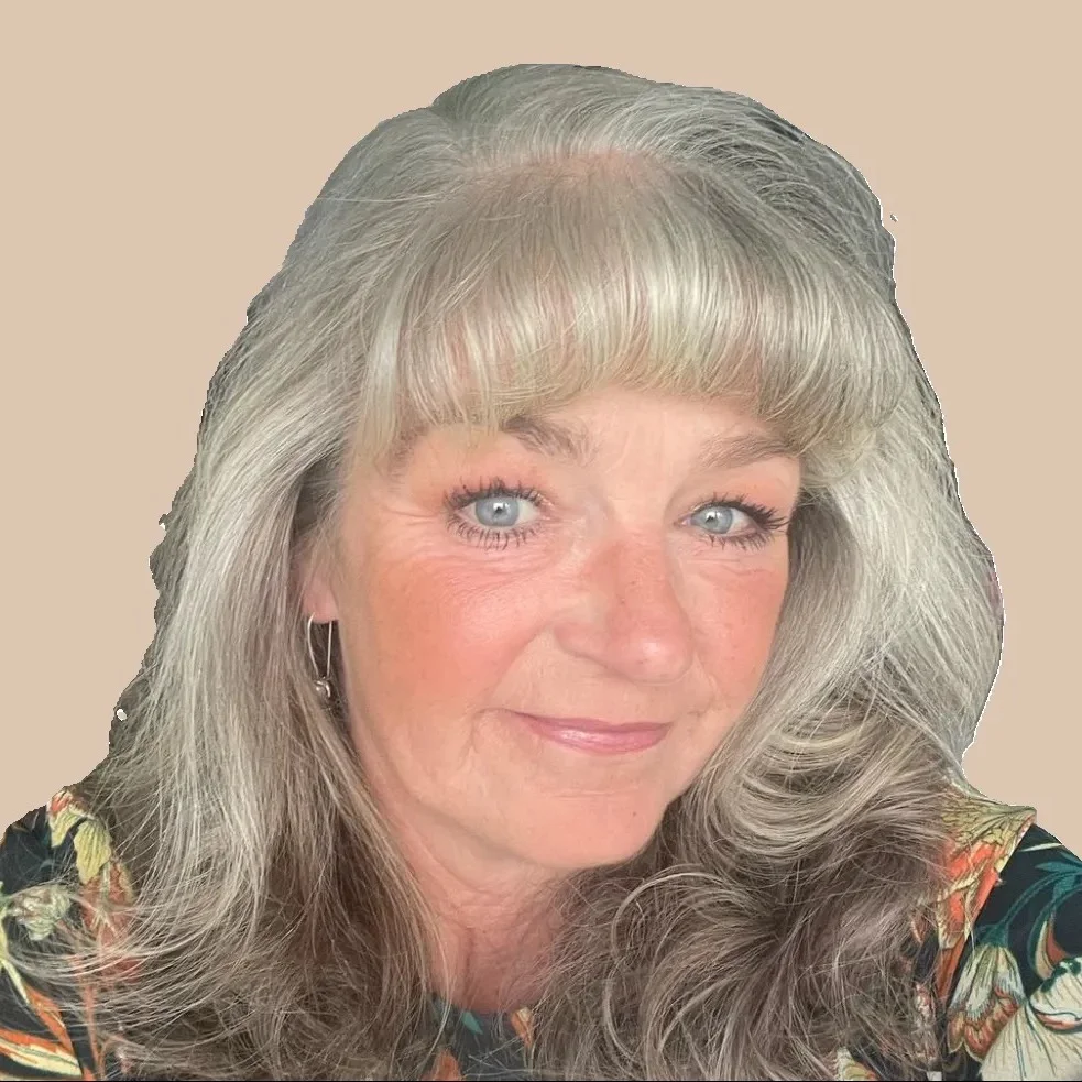 Woman with gray hair and blue eyes, wearing floral print top.