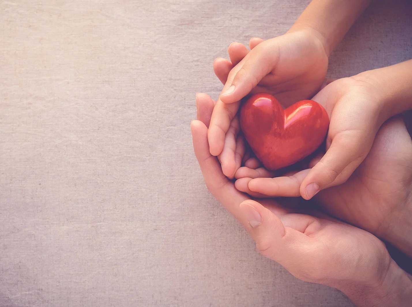 Adult and child hands cupping red heart.
