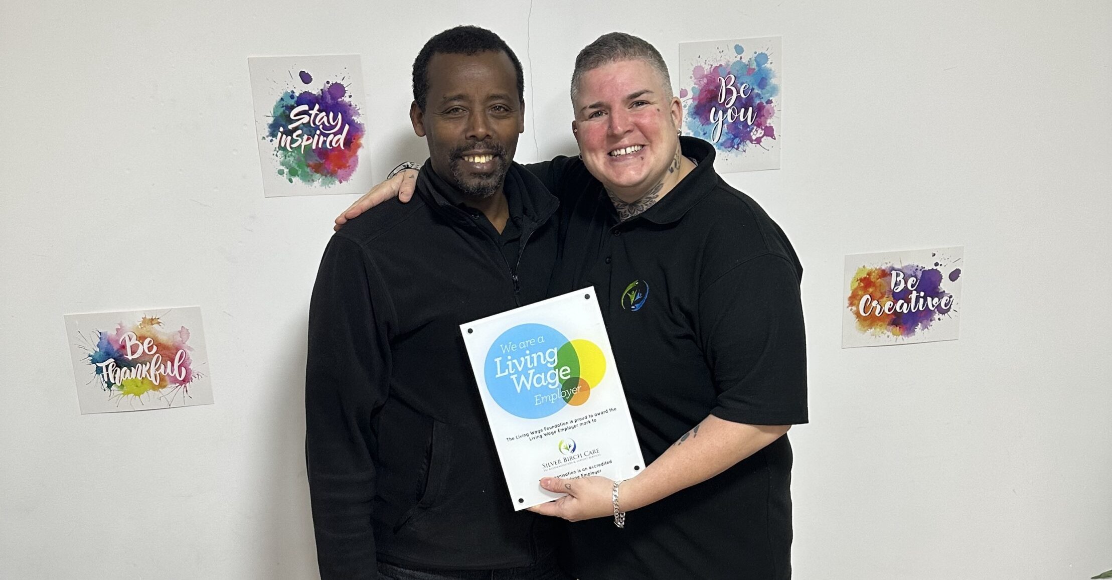 Two people holding a "Living Wage Employer" certificate.