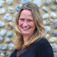 Sarah Porter with long blonde hair smiling in front of a stone wall.