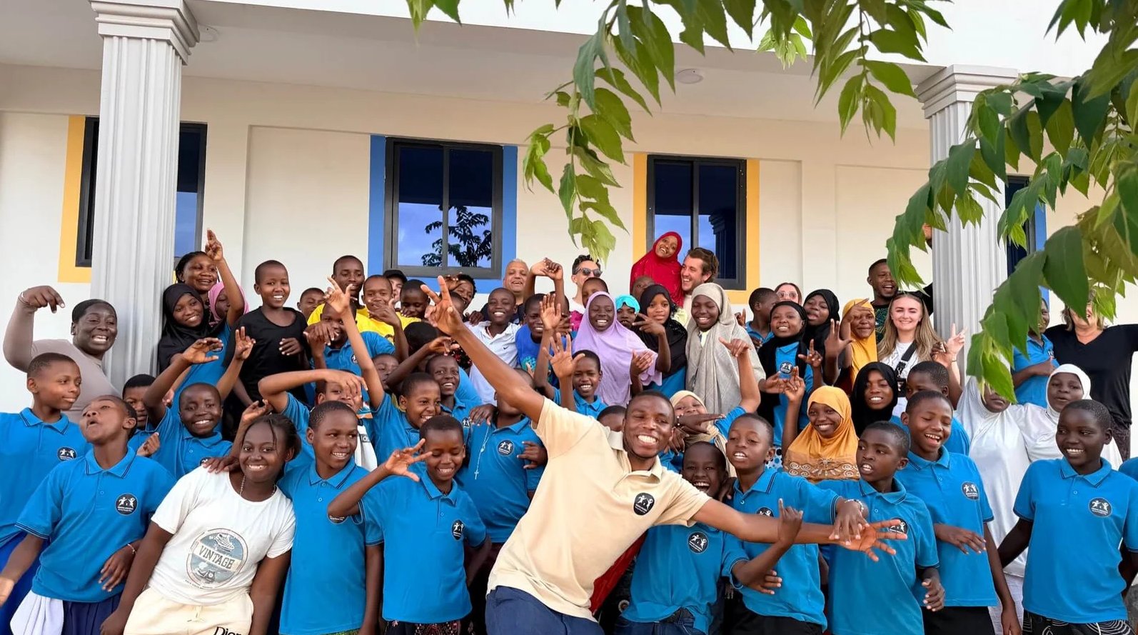 A large group of happy students in blue school uniforms posing with teachers in front of a school.
